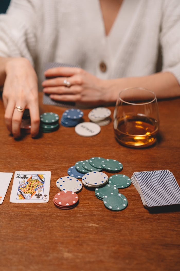 mobile-02 A close-up of a poker game setup on a wooden table with poker chips, cards, and a glass of whiskey.