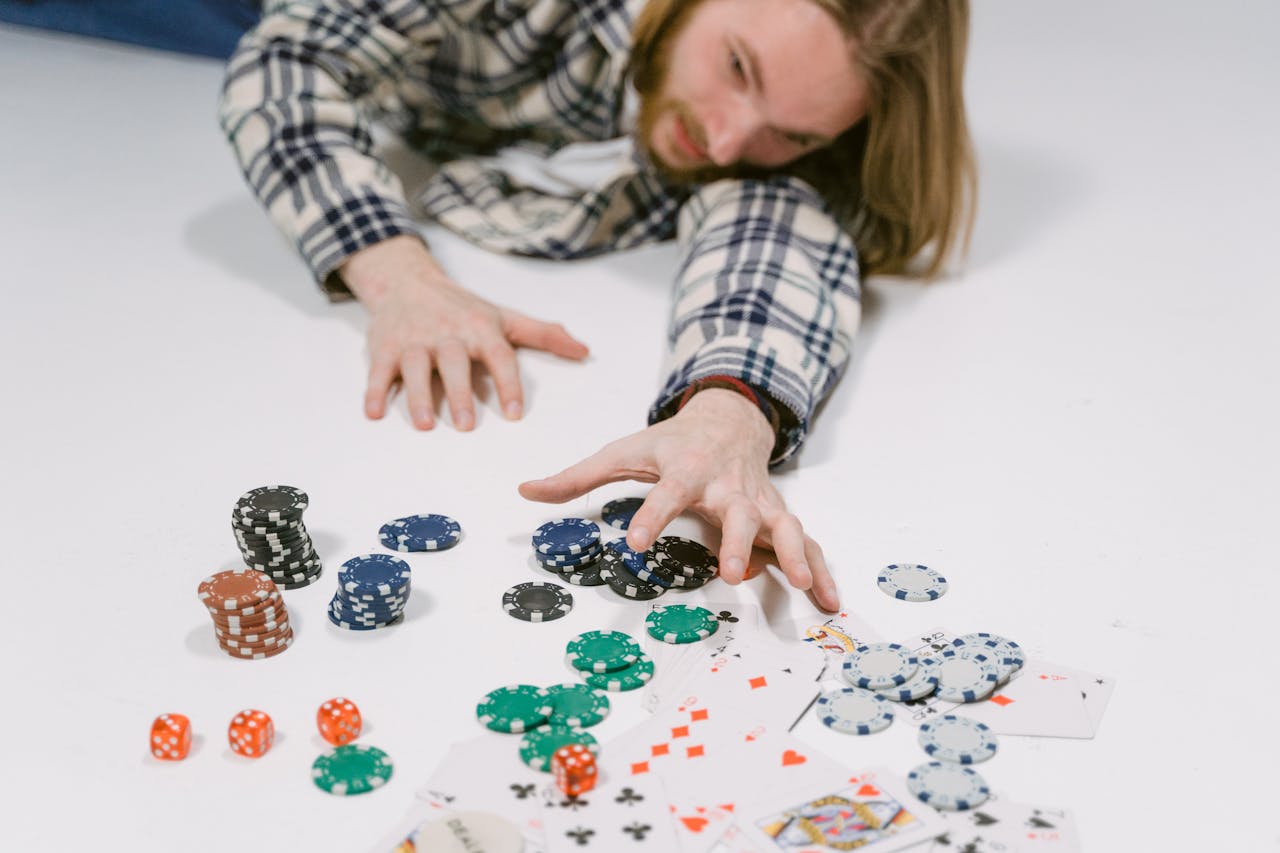 creative-03 A man in a plaid shirt reaches for poker chips on a white surface, depicting a gambling scene.