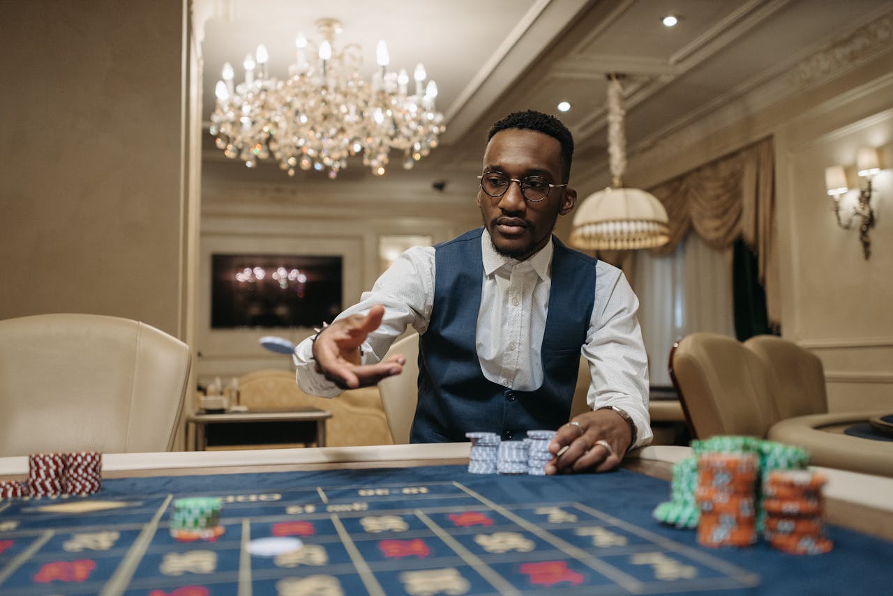 creative-03 A man in formal attire plays roulette in a luxurious casino under a chandelier.